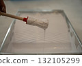 hand using a small round brush inside a plastic paint tray filled with white interior paint 132105299