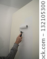 person painting an interior wall with a foam roller, applying a fresh white coat over a beige surface 132105300