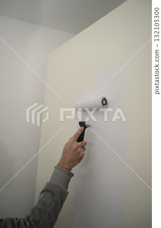 person painting an interior wall with a foam roller, applying a fresh white coat over a beige surface person painting an interior wall with a foam roller, applying a fresh white coat over a beige surface 132105300