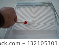 hand using a small round brush inside a plastic paint tray filled with white interior paint 132105301