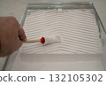 hand using a small round brush inside a plastic paint tray filled with white interior paint 132105302