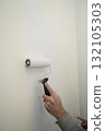 person painting an interior wall with a foam roller, applying a fresh white coat over a beige surface 132105303