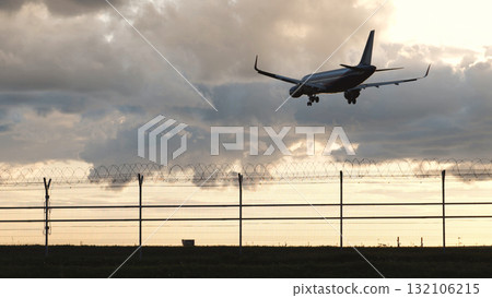 Passenger plane landing at airport behind barbed wire fence at sunset Passenger plane landing at airport behind barbed wire fence at sunset 132106215
