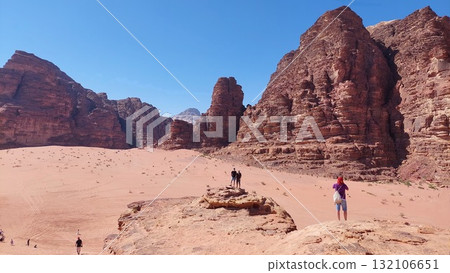 Tourists explore a vast red desert landscape surrounded by towering sandstone cliffs 132106651