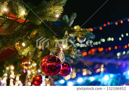 Christmas tree branch decorated with shiny red balls on glowing festive holiday lights background 132106952