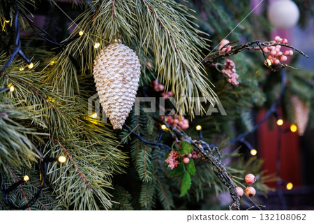 Festive pinecone decoration hangs among greenery and lights during the holiday season Festive pinecone decoration hangs among greenery and lights during the holiday season 132108062