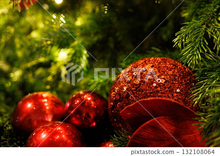 Sparkling red ornaments nestled among fresh green pine branches during the festive season 132108064
