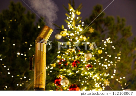 Brass pipe emitting steam near a beautifully decorated Christmas tree at night 132108067