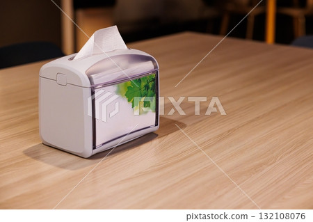 Decorative tissue box with leaf design on a wooden table in a cozy cafe setting 132108076
