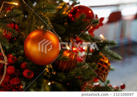 Brightly decorated Christmas tree adorned with shiny ornaments and warm lights in a cozy indoor setting 132108097