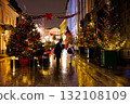 Festive scene of two people walking down a decorated street with Christmas lights and trees at night 132108109