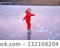 A child in a bright red jumpsuit learns to skate on the ice of a frozen lake 132108204