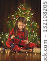 A sweet, beautiful girl with a smile unties a green bow on a Christmas box. Gifts from Santa Claus. 132108205