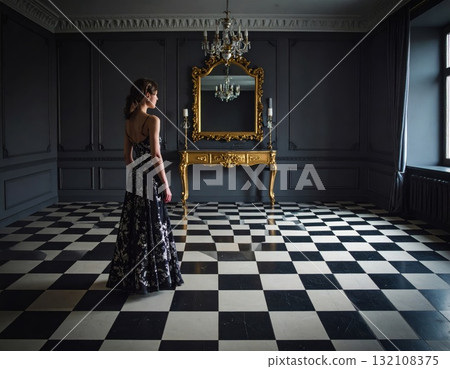 Woman in an evening dress standing on a checkered floor and looking into a mirror with a strange reflexion, conceptual horror scene Woman in an evening dress standing on a checkered floor and looking into a mirror with a strange reflexion, conceptual horror scene 132108375