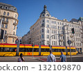 [Poland] An orange tram crosses a street in the capital, Warsaw, where historic buildings stand. 132109870