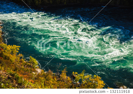 Powerful turquoise rapids of the Niagara River flowing between autumn-colored trees seen from above Powerful turquoise rapids of the Niagara River flowing between autumn-colored trees seen from above 132111918