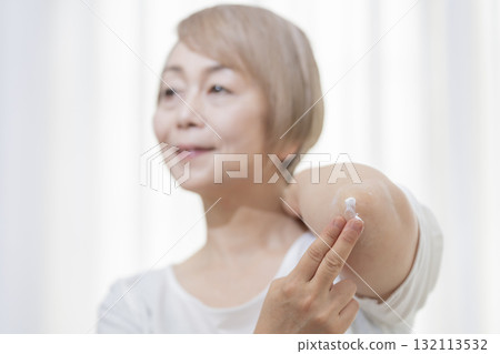 老年婦女在乾燥的肘部塗抹乳霜 132113532