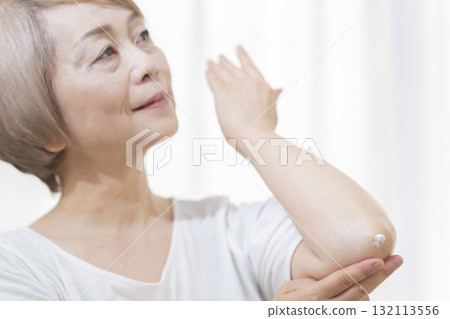 老年婦女在乾燥的肘部塗抹乳霜 132113556