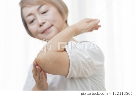 老年婦女在乾燥的肘部塗抹乳霜 老年婦女在乾燥的肘部塗抹乳霜 132113565