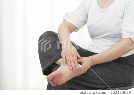 老年婦女在乾燥的腳跟上塗抹乳霜 老年婦女在乾燥的腳跟上塗抹乳霜 132113639