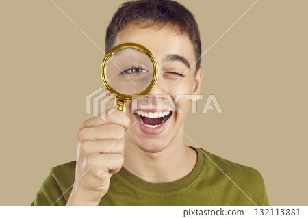 Boy looking through a magnifying glass isolated on a studio beige background. Boy looking through a magnifying glass isolated on a studio beige background. 132113881