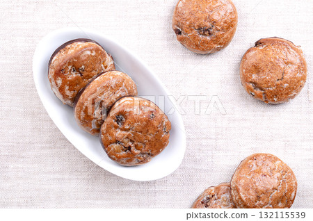 Fruit gingerbread, traditional German Lebkuchen in a white bowl, on linen. Christmas spice cookies, with candied fruit pieces, sugar glazed, dipped in dark chocolate at the bottom. Photo Fruit gingerbread, traditional German Lebkuchen in a white bowl, on linen. Christmas spice cookies, with candied fruit pieces, sugar glazed, dipped in dark chocolate at the bottom. Photo 132115539