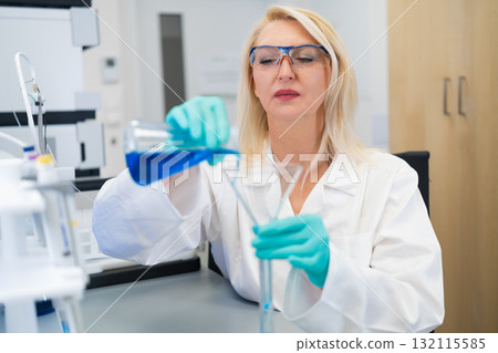 Woman scientist carefully pouring chemical solution through a glass funnel in a laboratory. Concept of precise scientific research, chemistry experiment, and modern laboratory techniques. Woman scientist carefully pouring chemical solution through a glass funnel in a laboratory. Concept of precise scientific research, chemistry experiment, and modern laboratory techniques. 132115585