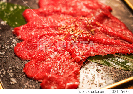 Raw beef slices with sesame seeds served on a black plate 132115624
