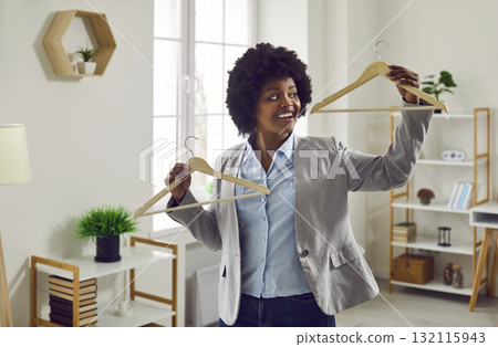 Happy, smiling young African American woman is holding two empty clothes hangers Happy, smiling young African American woman is holding two empty clothes hangers 132115943