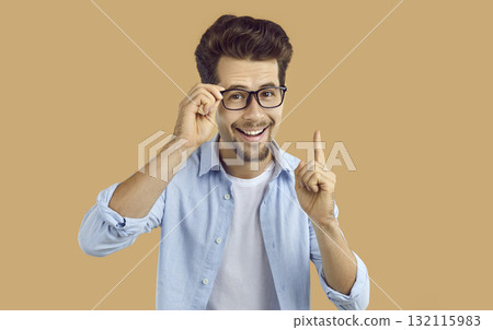 Clever young man in glasses has a good idea, smiles and points his index finger up 132115983