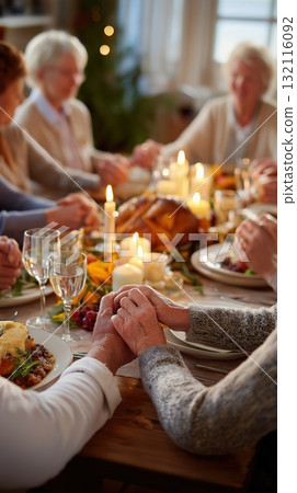 Family gathered around a festive dinner table holding hands in gratitude by candlelight 132116092