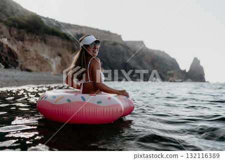 Woman, donut, sea. Happy woman relaxing on a fun float in the sea near rocky cliffs. 132116389