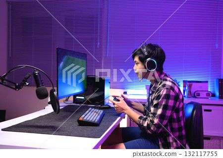 Young Asian gamer wearing headset playing video game at night with neon light, focused streaming setup and modern gaming lifestyle Young Asian gamer wearing headset playing video game at night with neon light, focused streaming setup and modern gaming lifestyle 132117755