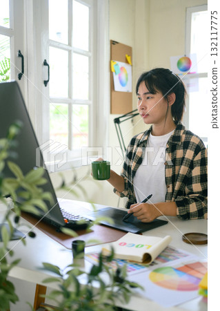 Graphic designer creating logo on digital tablet in bright modern workspace with computer and color palette Graphic designer creating logo on digital tablet in bright modern workspace with computer and color palette 132117775
