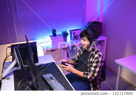 Young Asian gamer wearing headset playing video game at night with neon light, focused streaming setup and modern gaming lifestyle 132117800