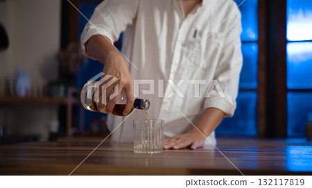 Man pouring whiskey into glass at night, warm light mood of relaxation and reflection. Man pouring whiskey into glass at night, warm light mood of relaxation and reflection. 132117819