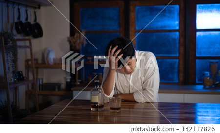Depressed man sitting alone with glass of alcohol at night, symbol of loneliness and stress Depressed man sitting alone with glass of alcohol at night, symbol of loneliness and stress 132117826