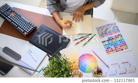 Top view creative woman sketching logo ideas in notebook with color samples and pencils Top view creative woman sketching logo ideas in notebook with color samples and pencils 132117865