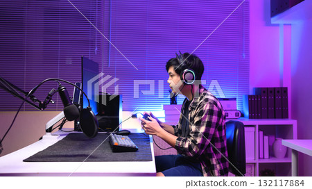 Young Asian gamer wearing headset playing video game at night with neon light, focused streaming setup and modern gaming lifestyle 132117884