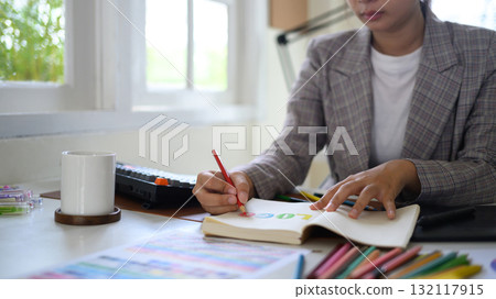 Closeup creative woman sketching logo ideas in notebook with color samples and pencils in bright modern workspace Closeup creative woman sketching logo ideas in notebook with color samples and pencils in bright modern workspace 132117915