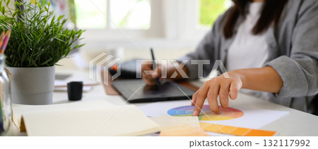 Cropped shot woman graphic designer creating logo on digital tablet in bright modern workspace with computer and color palette Cropped shot woman graphic designer creating logo on digital tablet in bright modern workspace with computer and color palette 132117992