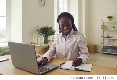 Happy African American businesswoman or college student using laptop and taking notes 132118920