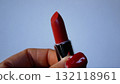 Woman's hand with red manicure holds and twists open a red lipstick. 132118961
