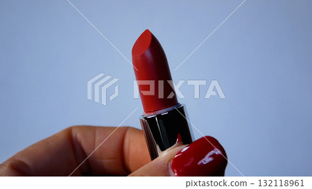 Woman's hand with red manicure holds and twists open a red lipstick. 132118961