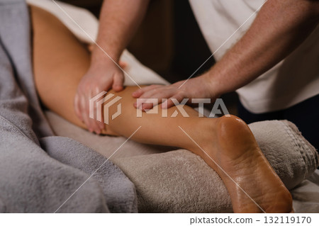 Massage therapy session focusing on relaxation and muscle relief in a serene spa environment, showcasing skilled hands working on a client's leg 132119170