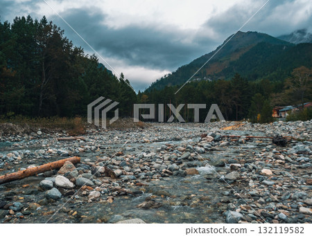 Serene river flowing through rocky landscape in mountains under overcast sky near forest 132119582
