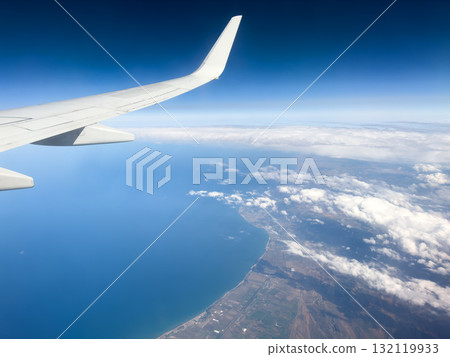 Aerial view of ocean through a plane window. Wing of airplane with blue sky and beauty clouds over the ocean. Aerial sea view Aerial view of ocean through a plane window. Wing of airplane with blue sky and beauty clouds over the ocean. Aerial sea view 132119933