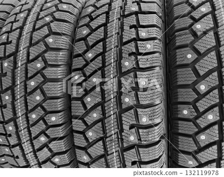 Winter studded tire. Winter car tires background. Tire stack background. Tyre protector close up. Square powerful spikes. Black studdable winter tyre profile. Car tires in a row 132119978