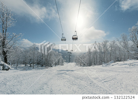 A ski lift moves upward through a winter landscape, surrounded by snow-covered trees and bright sunlight. A ski lift moves upward through a winter landscape, surrounded by snow-covered trees and bright sunlight. 132122524