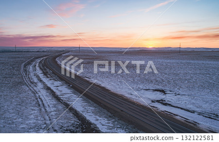 Snow-covered road stretches through a serene landscape at sunset in winter Snow-covered road stretches through a serene landscape at sunset in winter 132122581